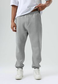 Grijze joggingbroek van een katoenmix, met een elastische tailleband, zijzakken, taps toelopende pijpen en geribbelde boorden. Draagt witte sneakers.