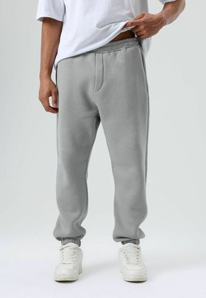 Grijze joggingbroek van een katoenmix, met een elastische tailleband, zijzakken, taps toelopende pijpen en geribbelde boorden. Draagt witte sneakers.