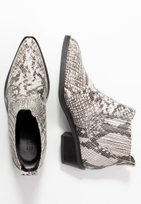 Stiefeletten mit einem glänzenden Schlangenhautmuster in Schwarz- und Weißtönen. Sie haben eine spitze Zehe, einen Blockabsatz und strukturierte Details.