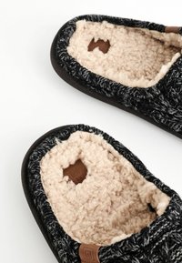 Black and gray knitted slippers with soft beige fleece lining and a brown label. Rounded shape with a textured, cozy appearance.