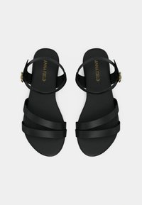 Sandales plates noires avec plusieurs fines brides et une boucle à la cheville. Matériau lisse, design minimaliste et semelle confortable.