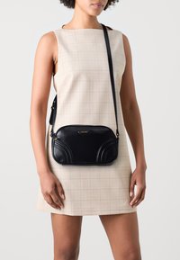 Borsa a tracolla in pelle nera con dettagli curvi, forma rettangolare e logo dorato. Tracolla regolabile e texture liscia.