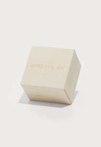Lys beige tekstureret smykkeboks med rektangulær form og let skråtaget låg. Har guldfolie prægede bogstaver: "GINETTE NY."