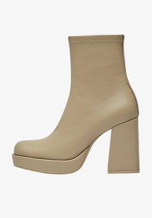 Bottine beige en cuir avec talon haut épais, bout arrondi, semelle plateforme et surpiqûres en zigzag le long du bord supérieur.