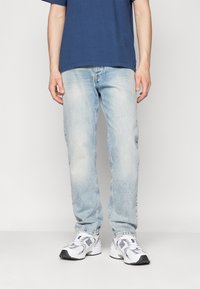 Jeans de denim de lavado claro con corte recto, textura ligeramente desvanecida, combinados con una camiseta azul marino y zapatillas deportivas blancas.