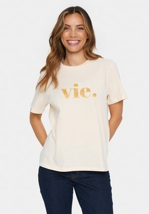 Crème kleurig katoenen t-shirt met glinsterende gouden tekst "vie." op de voorkant, ronde hals en korte mouwen. Combi met donkere jeans.
