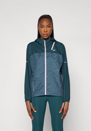 Veste coupe-vent turquoise avec un motif texturé sur le devant, fermeture éclair rose et capuche. Elle possède des manches longues et des accents réfléchissants.