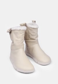 Botas de invierno de cuero beige con forro de suave piel, diseño ligeramente suelto, punta redonda y suela de goma texturizada. Con bucles en la parte posterior como acento.