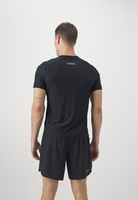 Camiseta atlética negra de manga corta y escote redondo, combinada con pantalones cortos a juego. Presenta un logotipo reflectante en la parte posterior.