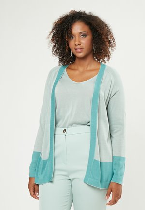 Cárdigan ligero en azul claro con acentos en verde azulado, con un ajuste relajado, manga larga y una textura suave. Combinado con pantalones en tonos pastel.