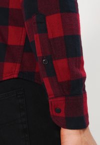 Czerwona i granatowa koszula flanelowa w kratę, z mankietem zapinanym na guziki, miękką fakturą i kontrastującymi kolorami w odważnym wzorze w kratę.