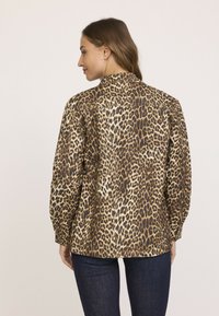 Blouse imprimé léopard avec col, manches longues et coupe décontractée. Le tissu présente une texture brillante avec des nuances de brun et de crème.