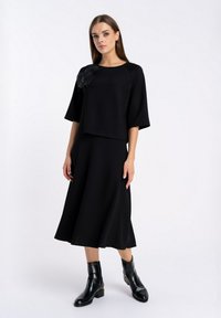 Czarna dwuczęściowa sukienka składająca się z krótkiego topu z rękawami do trzech czwartej oraz rozkloszowanej spódnicy, ozdobiona kwiatowym akcentem na ramieniu.