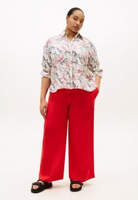 Ελαφρύ πουκάμισο με κουμπιά και σχέδιο σε παστέλ αποχρώσεις, συνδυασμένο με ζωηρά κόκκινα παντελόνια με φαρδιά πατζάκια και μαύρα σανδάλια. Διαθέτει άνετη εφαρμογή και τσέπες.
