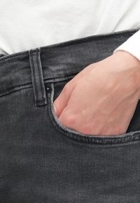 Šedé džíny z denimu s viditelnou přední kapsou, mají čistý design a detailní švy. Ruka spočívá uvnitř kapsy.