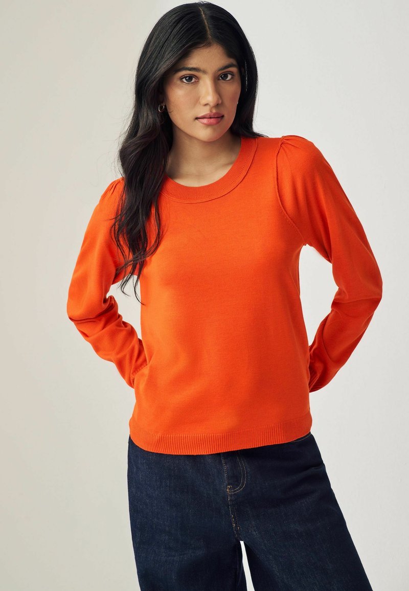 Pullover arancione a maglia con maniche lunghe, scollo rotondo e orlo a coste. Presenta dettagli a sbuffo sui cuciture delle spalle.