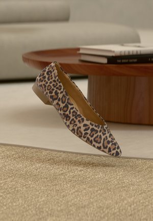 Ploché boty se vzorem leopardí kůže, s špičatou špičkou a nízkým podpatkem, vznášející se nad béžovým texturovaným kobercem v moderním obývacím pokoji.