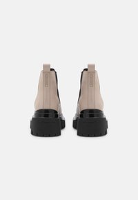 Bottines noires et beiges avec une semelle épaisse, en cuir lisse et panneaux latéraux élastiques, dotées d'une languette à l'arrière et d'un détail de logo.