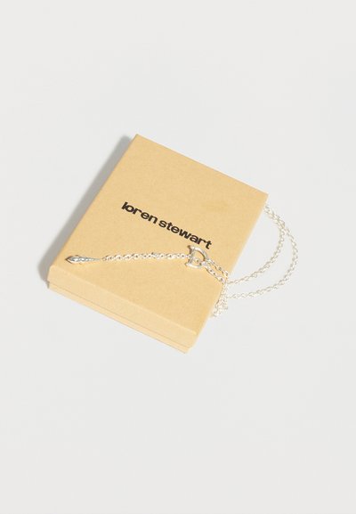 Ασημένιο κολιέ αλυσίδα με κούμπωμα toggle, τοποθετημένο πάνω σε ένα μπεζ κουτί με την ετικέτα «loren stewart», σε λευκό φόντο.