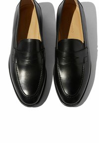 Zwarte leren instappers met een strak ontwerp, ronde neus en subtiele stikseldetails. Vloeiende textuur met een gepolijste afwerking, voorzien van een bandaccent.