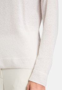 Jasnokremowy sweter z dzianiny z prążkowanym dołem. Miękka faktura, lekko luźny krój, widoczne szwy oraz szerokie mankiety.