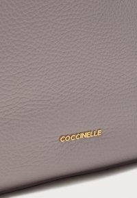 Γκρι πορτοφόλι από δερμάτινη υφή με ανάγλυφο χρυσό λογότυπο, που τονίζει ένα λείο, ανθεκτικό φινίρισμα και έναν διακριτικό χρωματικό τόνο.