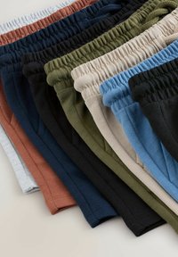 Rugalmas derékpántokból álló halom összehajtott pamut nadrágokban, szürke, rozsdabarna, tengerészkék, fekete, olívazöld, bézs, világoskék és fekete színekben.