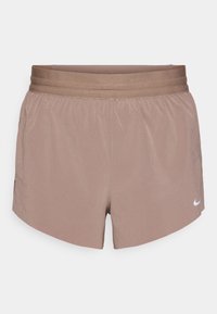Bruine sportshorts met een elastische tailleband. Bijna gladde textuur, zijsplitten voor bewegingsvrijheid en een klein wit logo aan de onderkant rechts.