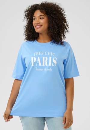 Svetlo modra majica s kratkimi rokavi, ki vsebuje bel napis "TRÈS CHIC PARIS" in "Toujours à la mode" v sproščenem dizajnu.