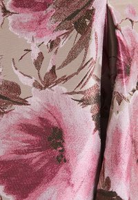 Tissu floral présentant de grandes fleurs roses et bordeaux sur un fond beige texturé. Des accents de fils métalliques ajoutent de la profondeur.