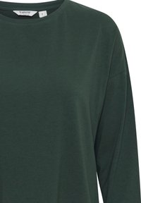Donkergroene langemouwen t-shirt van zacht, lichtgewicht stof. Bevat een ronde hals en een losse fit, met een zichtbare labeltag.