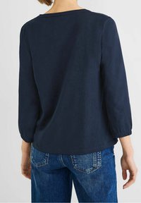 Marinblus med trekvartslånga ärmar, elastiska manschetter och rundad halsringning, i kombination med ljusblå denimjeans.