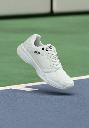 Valge FILA spordijalanõud hõljuvad sinise ja rohelise tennisekihi kohal piirijoone lähedal.