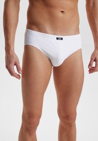 Witte katoenen slips met een klassieke snit, voorzien van een elastische tailleband en een klein zwart label aan de voorkant. Gladde textuur, geen zichtbare patronen.