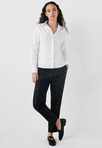 Camicia bianca con colletto, abbinata a pantaloni neri aderenti e mocassini neri con dettagli dorati. Design semplice e sartoriale.