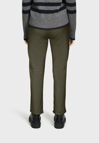 Pantalons vert olive en tissu lisse, dotés d'une coupe droite, portés avec un pull rayé gris et des chaussures à semelle épaisse noires.