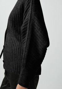 Schwarzer gerippter Pullover mit strukturiertem Oberflächenmaterial, der ein weites, lässiges Design, schlabberige Ärmel und Knopf-Akzente an der Seite aufweist.
