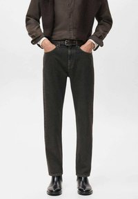 Jeans verde oscuro con un diseño de pierna recta, hechos de denim. Presentan bolsillos laterales y un cinturón, combinados con botas negras hasta el tobillo.