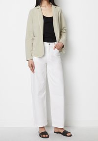 Jasnobeżowa marynarka z klapami z wycięciem, czarny top na ramiączkach, białe spodnie o szerokich nogawkach oraz czarne klapki, na jednolitym tle.