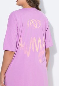 Lila oversized t-shirt met korte mouwen. Heeft een gradient oranje grafisch ontwerp op de achterkant, met een soepele katoenen textuur.