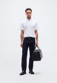 Ανοιχτό μπλε πουκάμισο με κουμπιά, σκούρο τζιν, μαύρα επίσημα παπούτσια και μια δομημένη μαύρη δερμάτινη τσάντα με χερούλια. Το πουκάμισο έχει κοντά μανίκια.