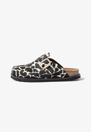 Clog slip-on con stampa animalier bianca e nera, cinturino con fibbia dorata, sottopiede in sughero e suola in gomma nera su sfondo bianco.