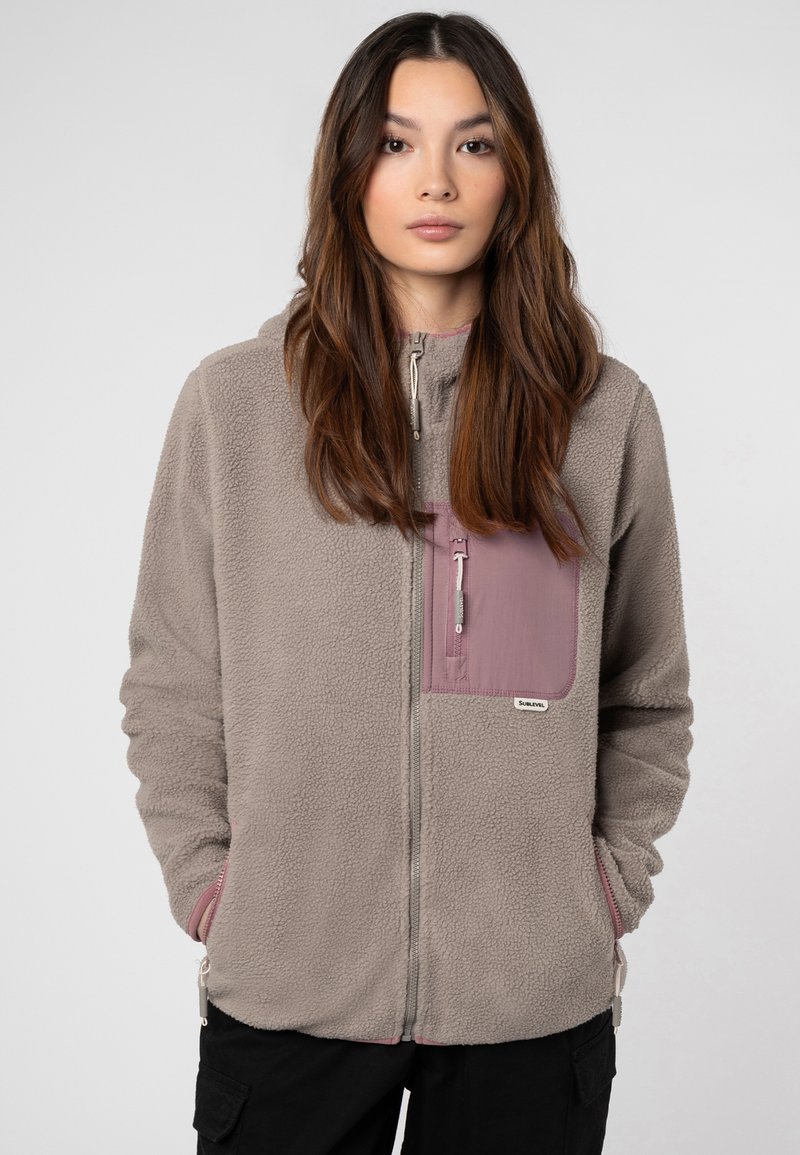 Gray fleece jacket with a zippered front, a mauve chest pocket, and elastic cuffs. Features branded label on the pocket and soft texture.