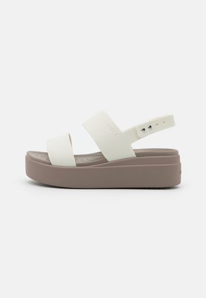 White strap sandals with a wide, slightly textured midsole and a tan platform. Features adjustable heel strap with multiple size holes.