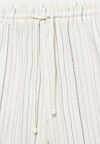 Pantalon en tissu blanc avec de fines rayures noires verticales et une ceinture à cordon nouée en nœud devant, au centre.