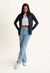 Marineblaues Zip-Up-Jackett mit langen Ärmeln und Logodetail, kombiniert mit hellblauen Sweatpants. Strukturiertes Material, lockere Passform und knöchellanges Design.