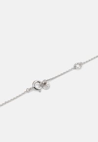 Silberne Kettenarmband mit einem runden Verschluss, ausgestattet mit einem kleinen Anhänger mit zwei runden Scheiben, von denen eine mit klaren Steinen verziert ist.