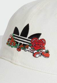 Gorra blanca con logotipo bordado en negro que presenta tres rayas. Diseño floral colorido y un personaje de oso rojo con espirales. Tela texturizada.