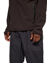 Personne portant un haut noir à manches longues avec une poche zippée sur la manche et un pantalon noir ample avec des poches visibles.