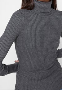 Harmaa, ribbineulottu pooloneule pitkähihaisilla, istuvalla mallilla ja hieman paksummalla neuloksella lämmön takaamiseksi.